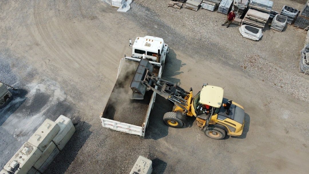 Loader filling a dump truck with dark aggregate in a logistics yard
